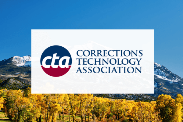 The image shows a large white sign with the logo and name of the "Corrections Technology Association" against a backdrop of a mountainous landscape with colorful autumn foliage in the foreground.