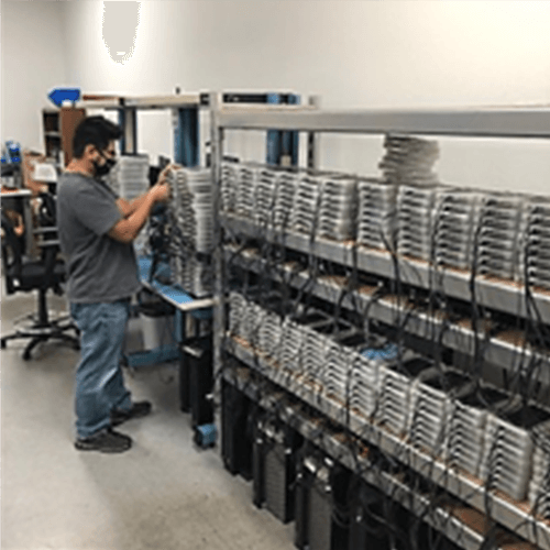 The image shows a person working on a large server rack filled with various electronic components and devices.