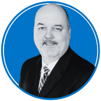 The image shows a middle-aged man with a bald head and a friendly smile, wearing a black suit and tie against a bright blue background.