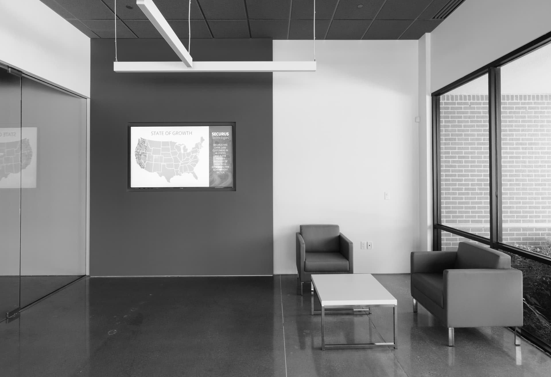 A modern, minimalist office space with a gray and white color scheme, featuring a framed artwork on the wall, a couch, and a coffee table in the foreground.