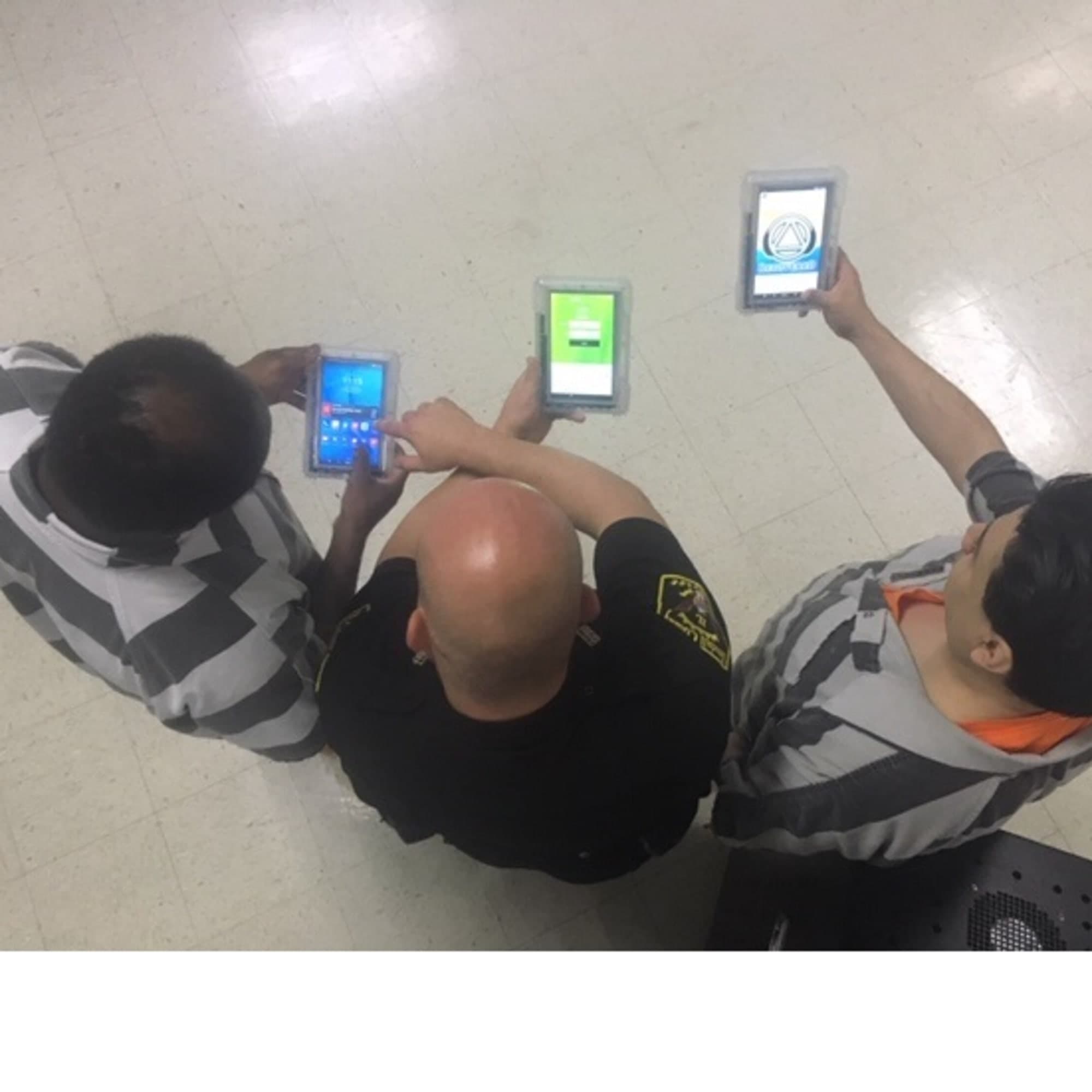 The image shows two individuals in uniform, one holding a mobile device and the other reaching towards a wall-mounted device.