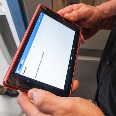 A person's hands are holding a red tablet device displaying a white screen with text.